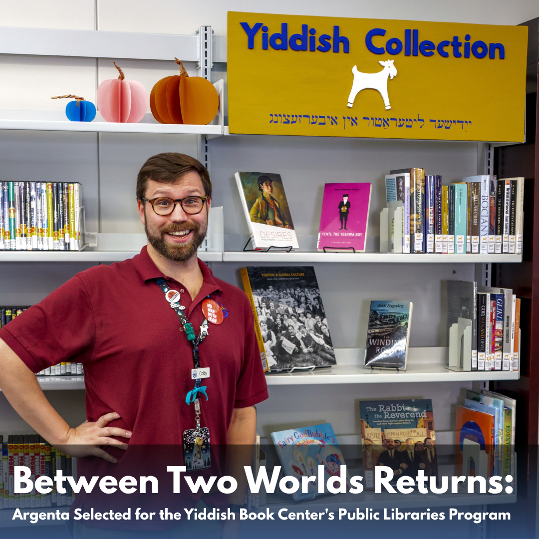 Colby Sansom stands beside the Yiddish Collection shelves at Argenta Public Library. Text: Between Two Worlds Returns: Argenta Selected for the Yiddish Book Center's Public Libraries Program.