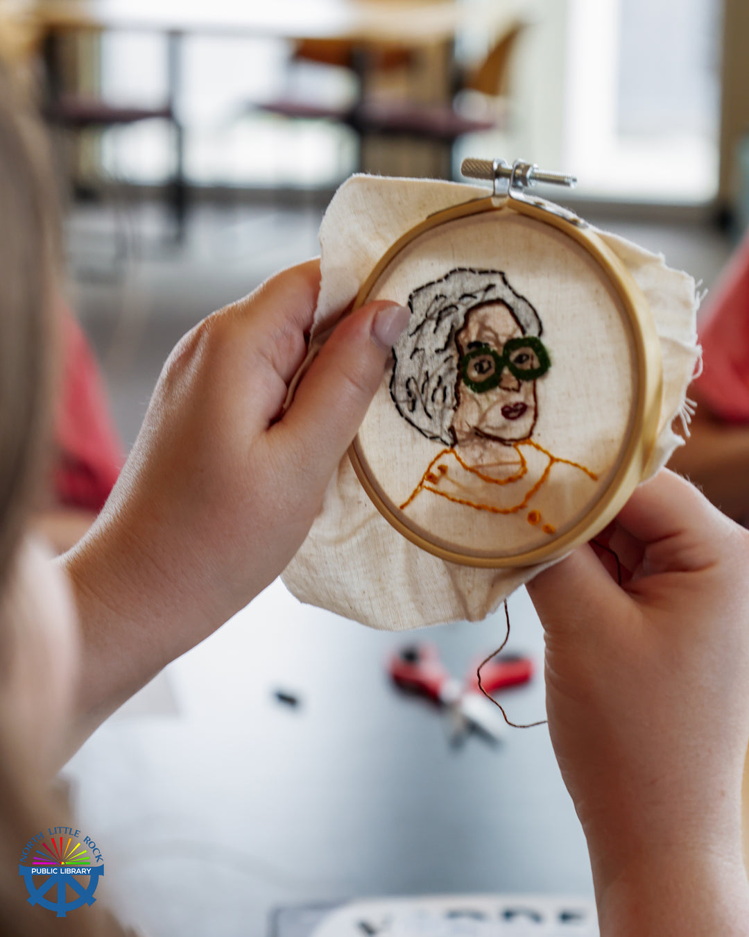 A library patron works on an embroidered portrait of Mary Jackson, one of the titular Hidden Figures.