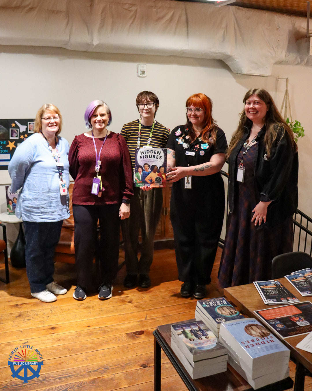 A group of library staff members pose with a copy of Hidden Figures at the One Community, One Book kickoff event at Blackberry Market.