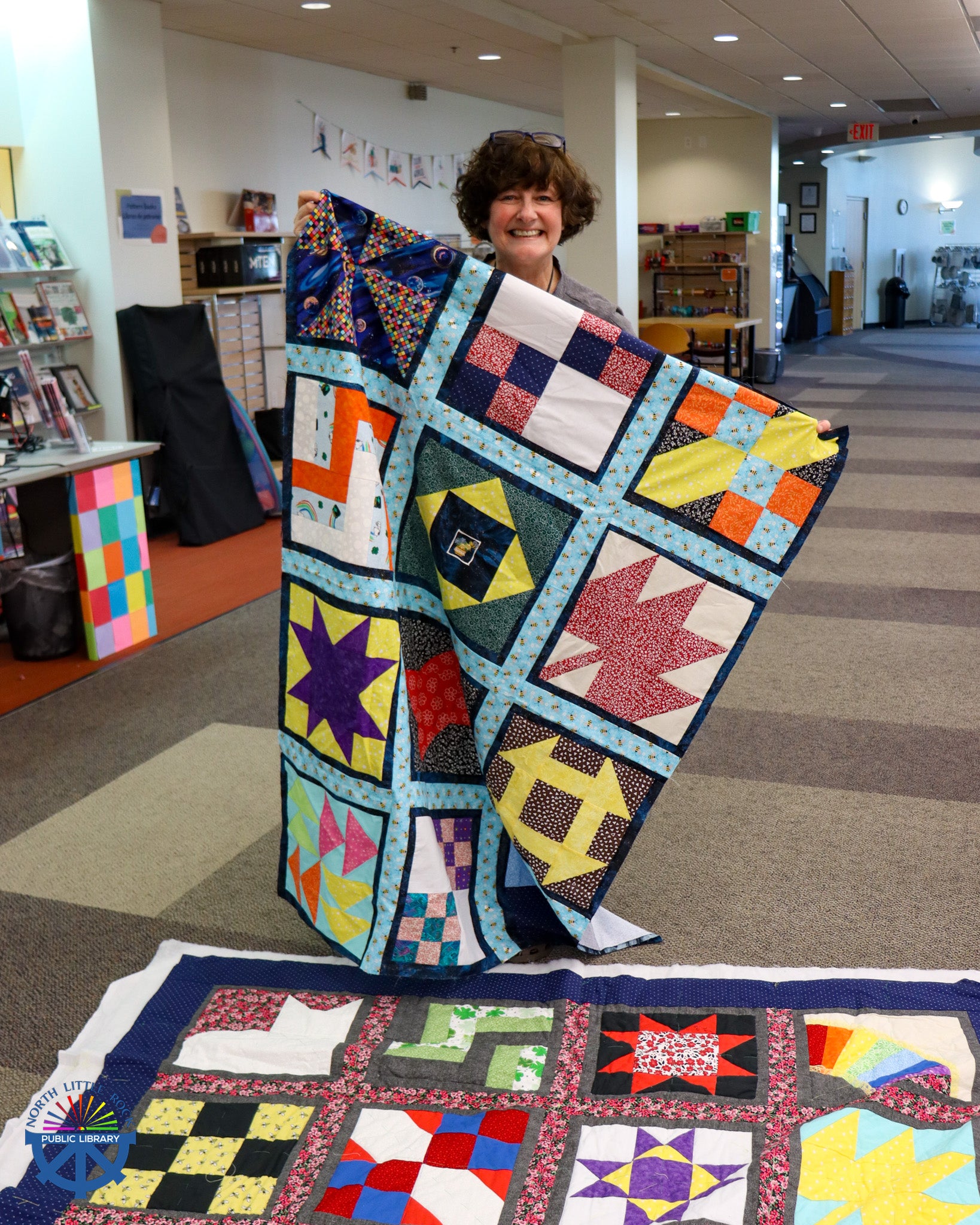 A smiling person holding a colorful quilt.