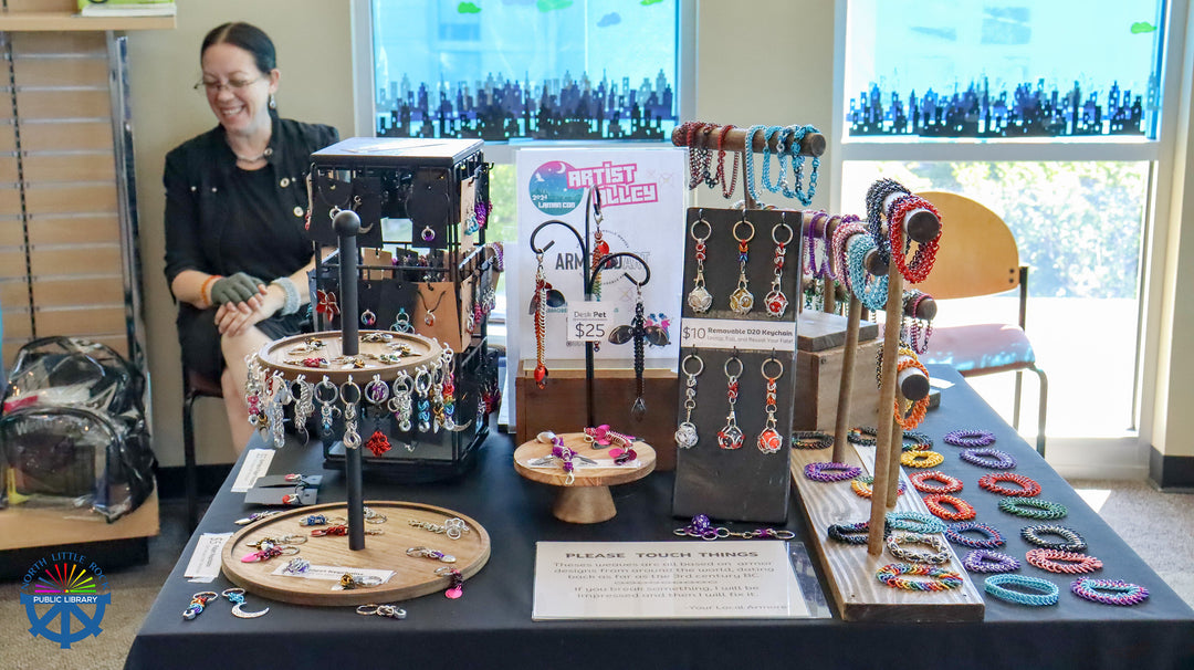 Person standing behind a table displaying various chainmaille handcrafted  jewelry items in the library rotunda.