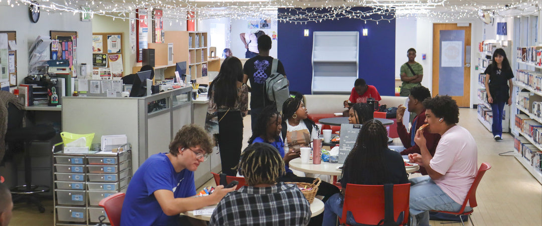 Teens sitting at tables socializing in a narrow room with string lights hung from the ceiling.