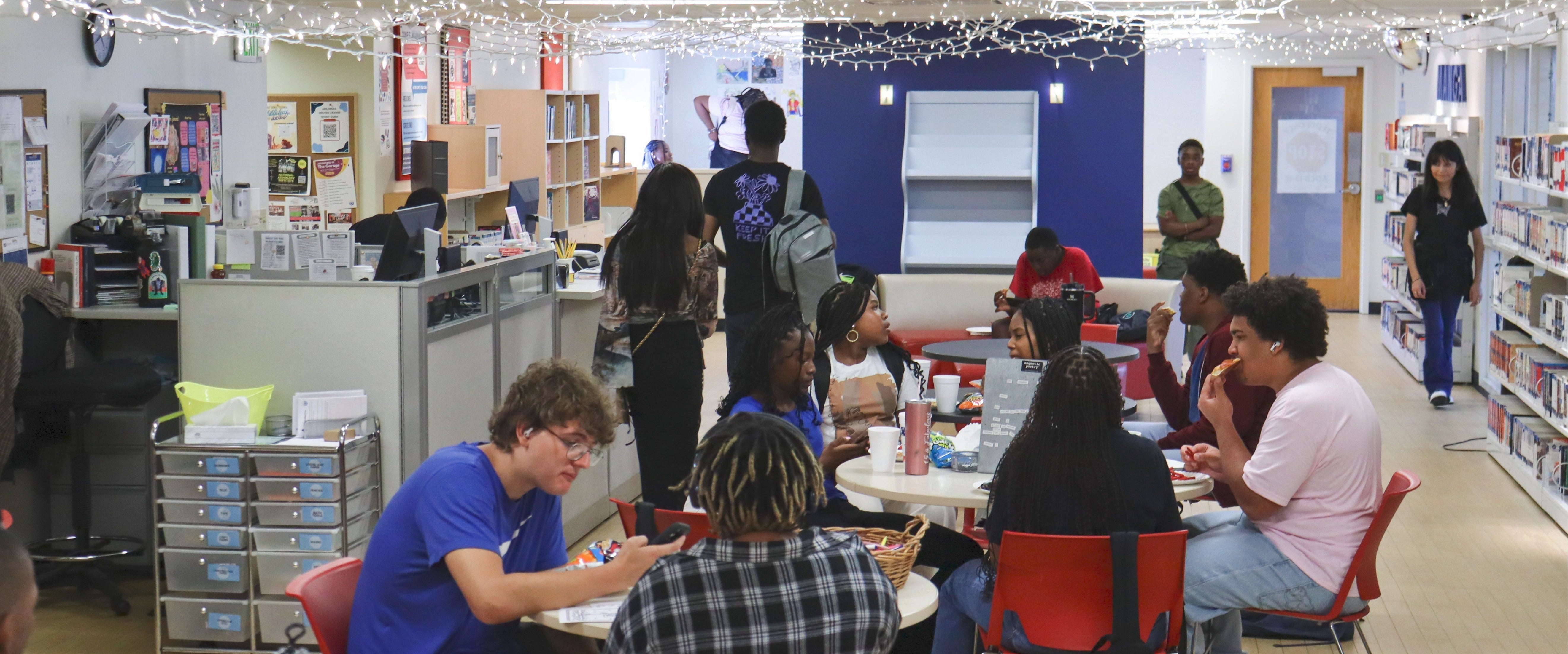 Teens sitting at tables socializing in a narrow room with string lights hung from the ceiling.