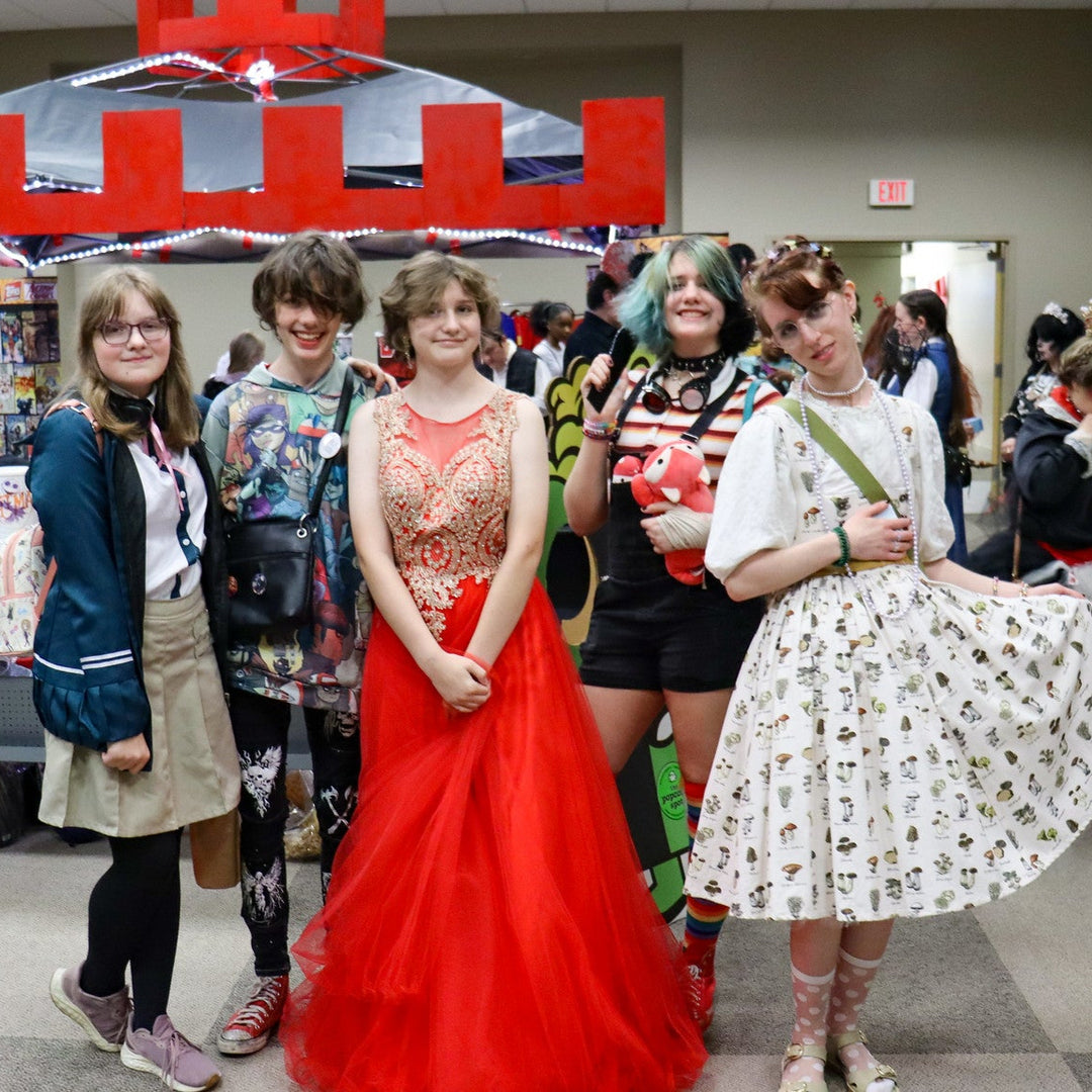 Group of people in cosplay posing together in the Vendor alley of Laman Con 2024  with a red and gray castle booth in the background.