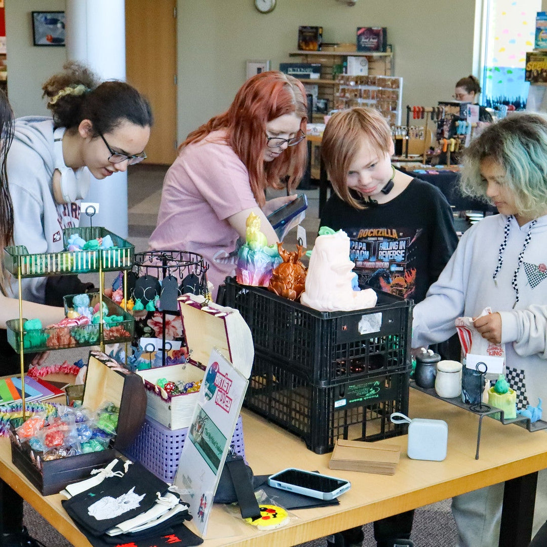 Group of people gathered around a table with various 3d printed comicon items at Laman Con