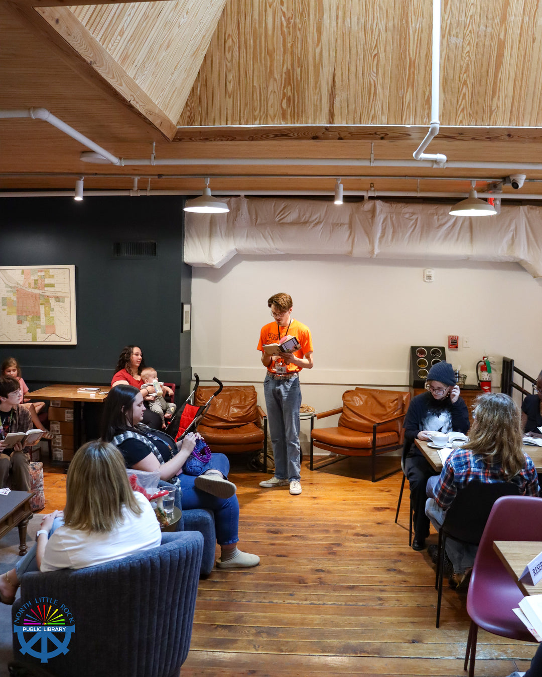 Lewis giving a short live reading of the book in a casual setting with attendees seated on chairs and couches.