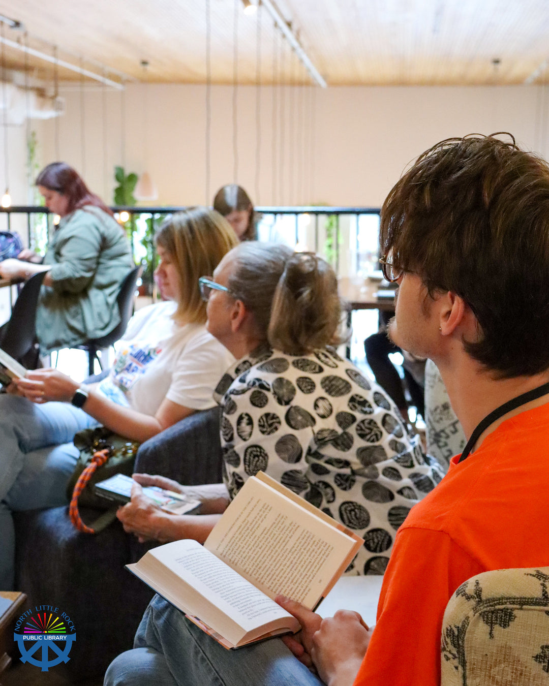 People sitting in a room, some reading books, with a casual atmosphere.
