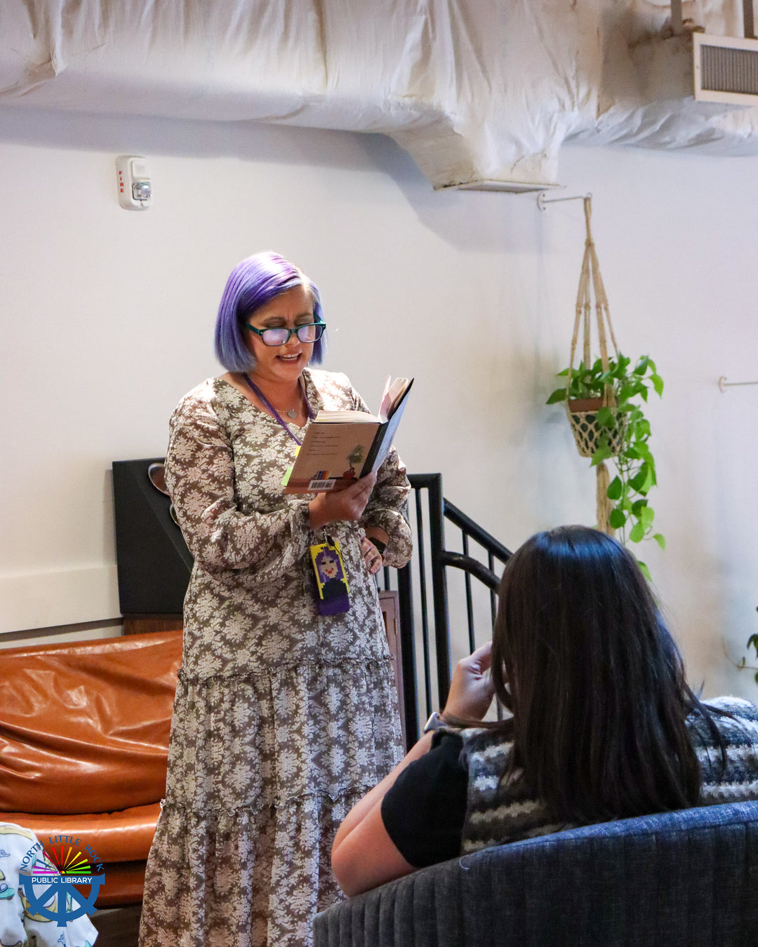 Twyla with her signature purple hair reading a book to another person in a casual setting at Blackberry Market in Argenta
