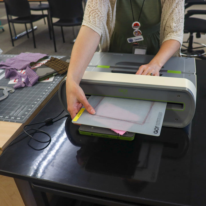 A person using an Accuquilt machine to cut out fabric.