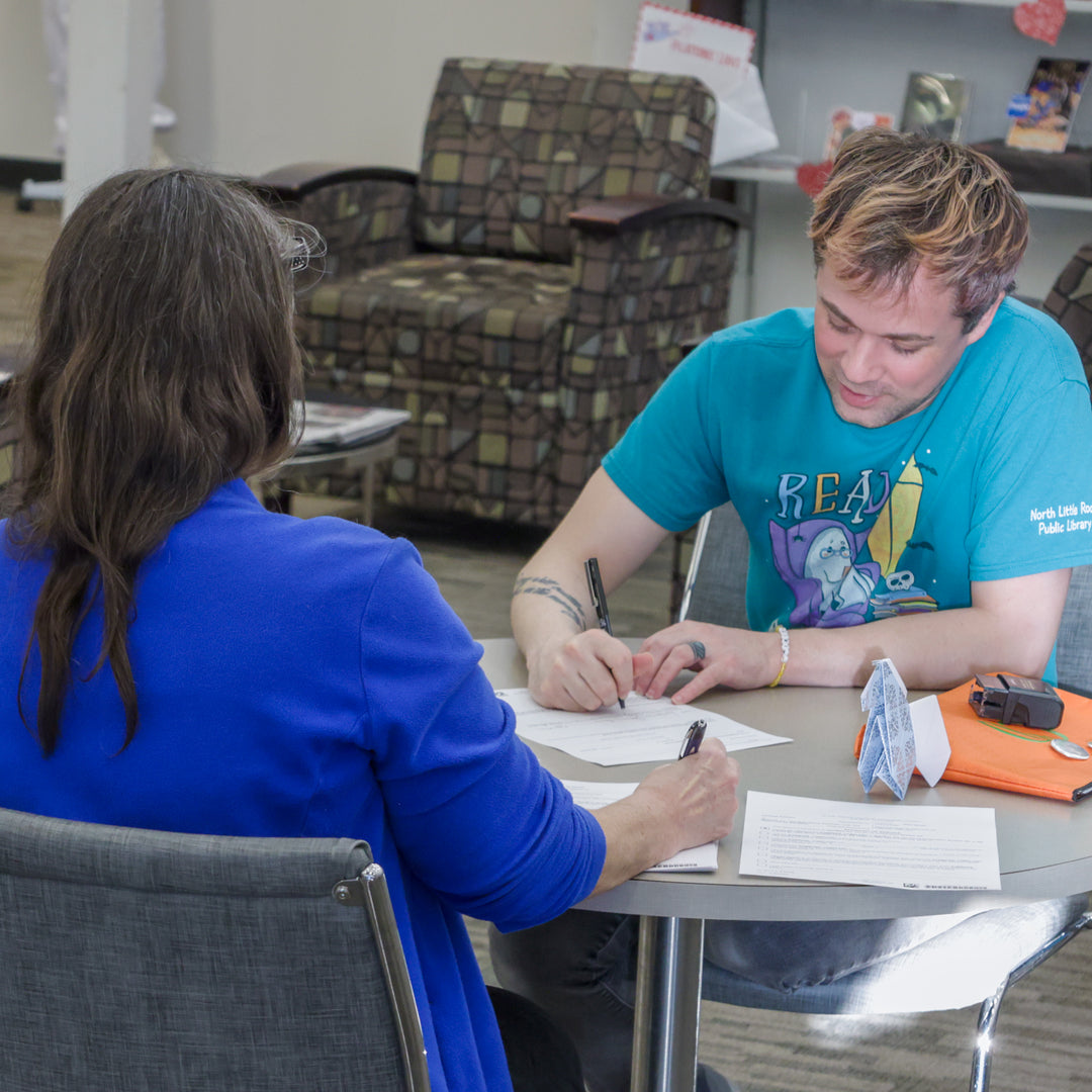A staff member in a teal shirt notarizes a document for a patron in a blue shirt.