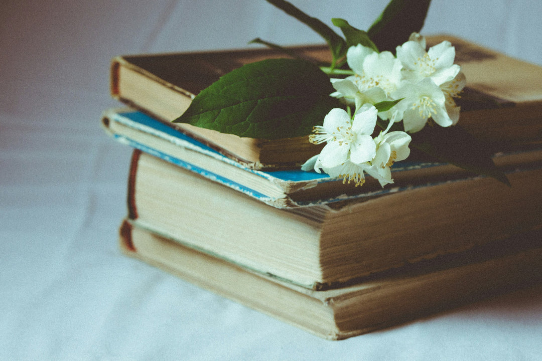 A stack of four antique books with a sprig of white flowers resting on top.