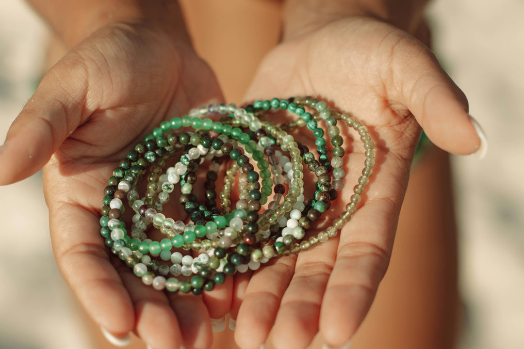A person holding out a handful of green beaded bracelets.