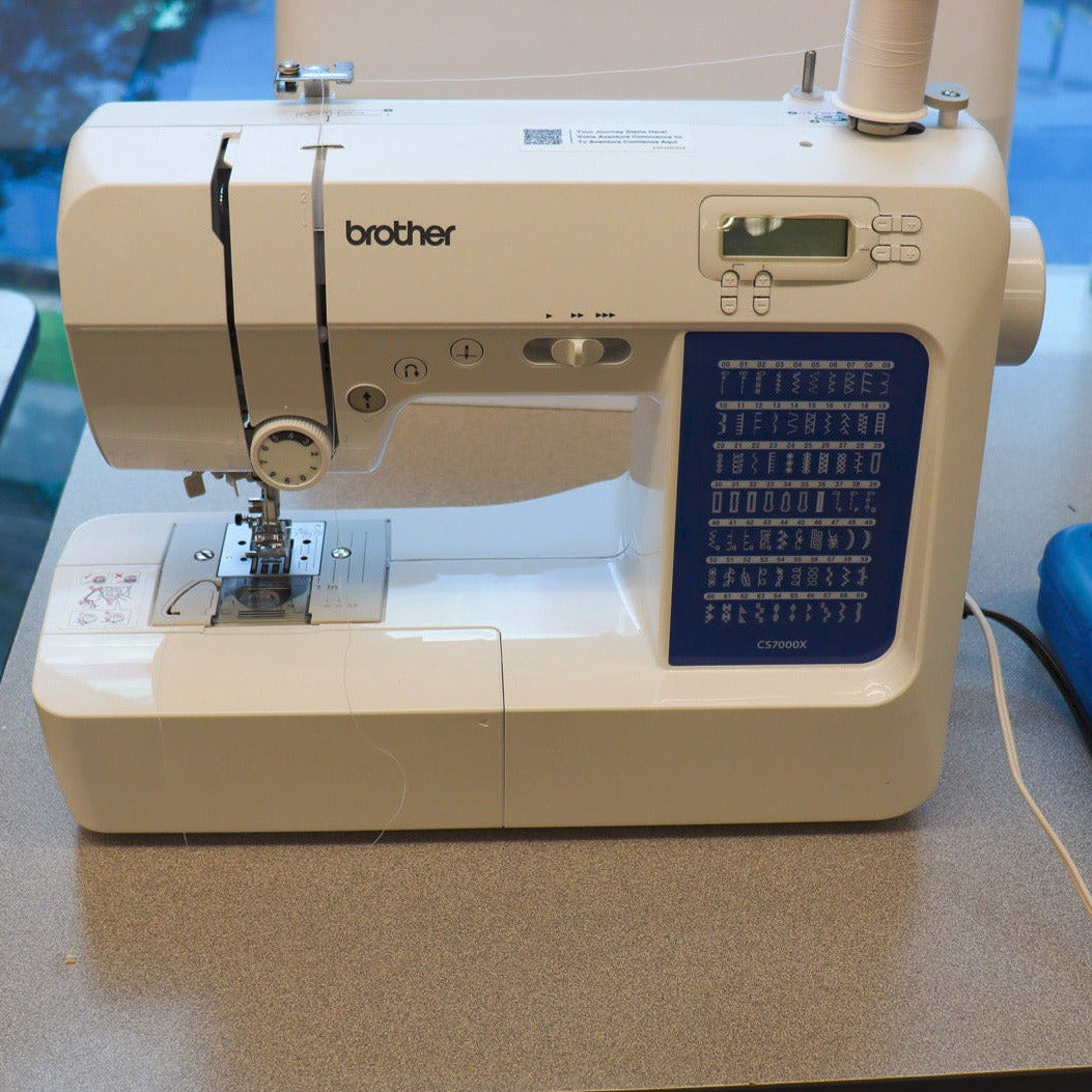 Brother sewing machine on a counter with a blue box of sewing tools.