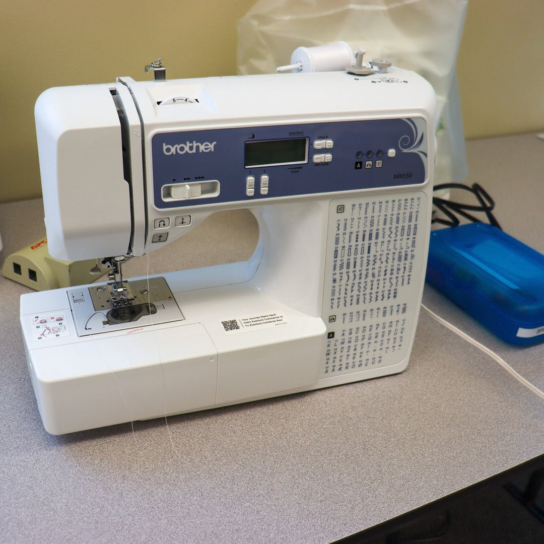 Brother sewing machine on a counter with a blue box of sewing tools.