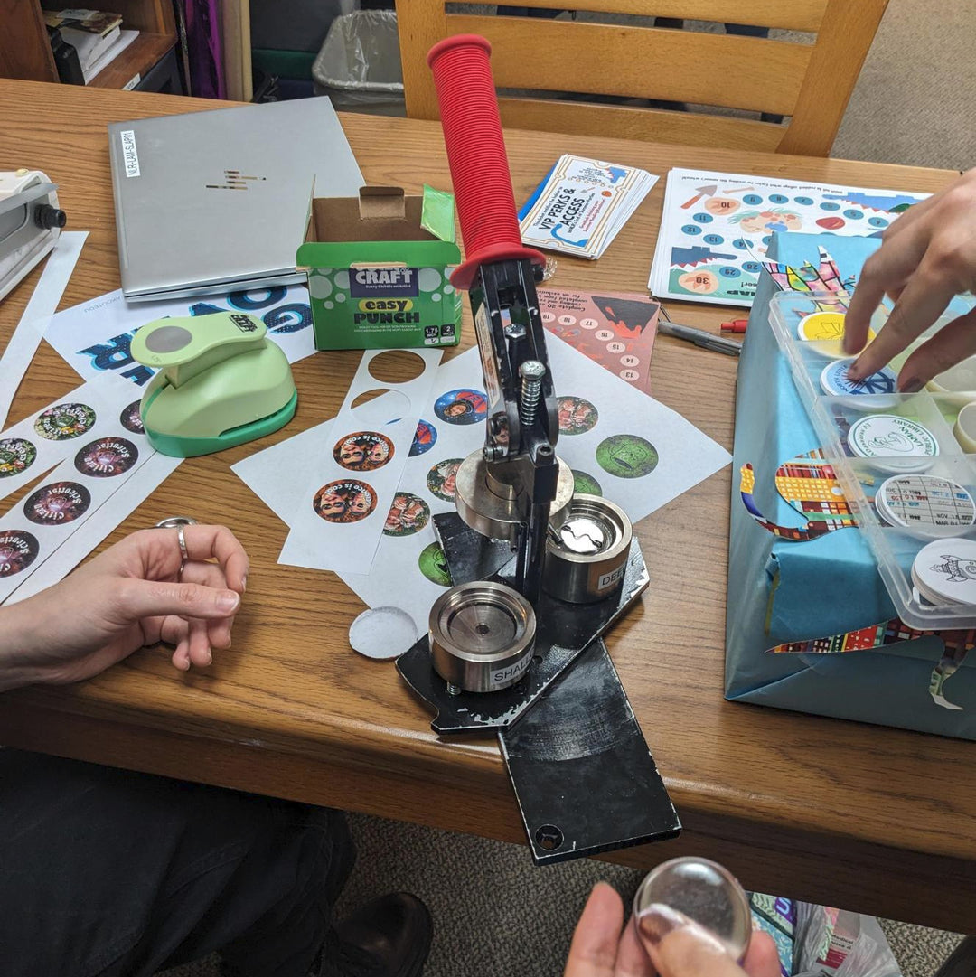 An industrial button maker being used on a wooden table.