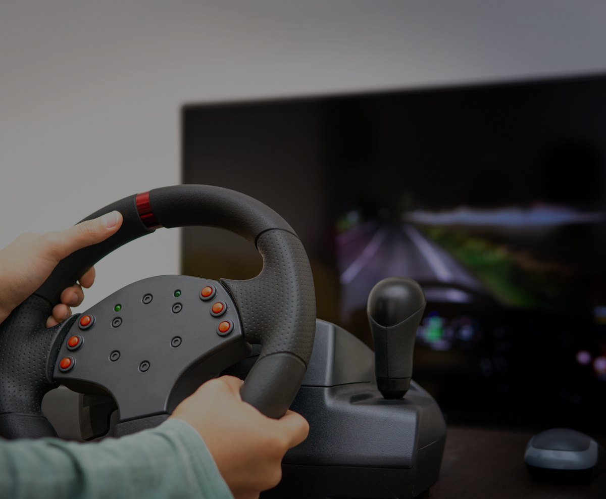 A person holding a wheel in front of a screen showing a view of a road.