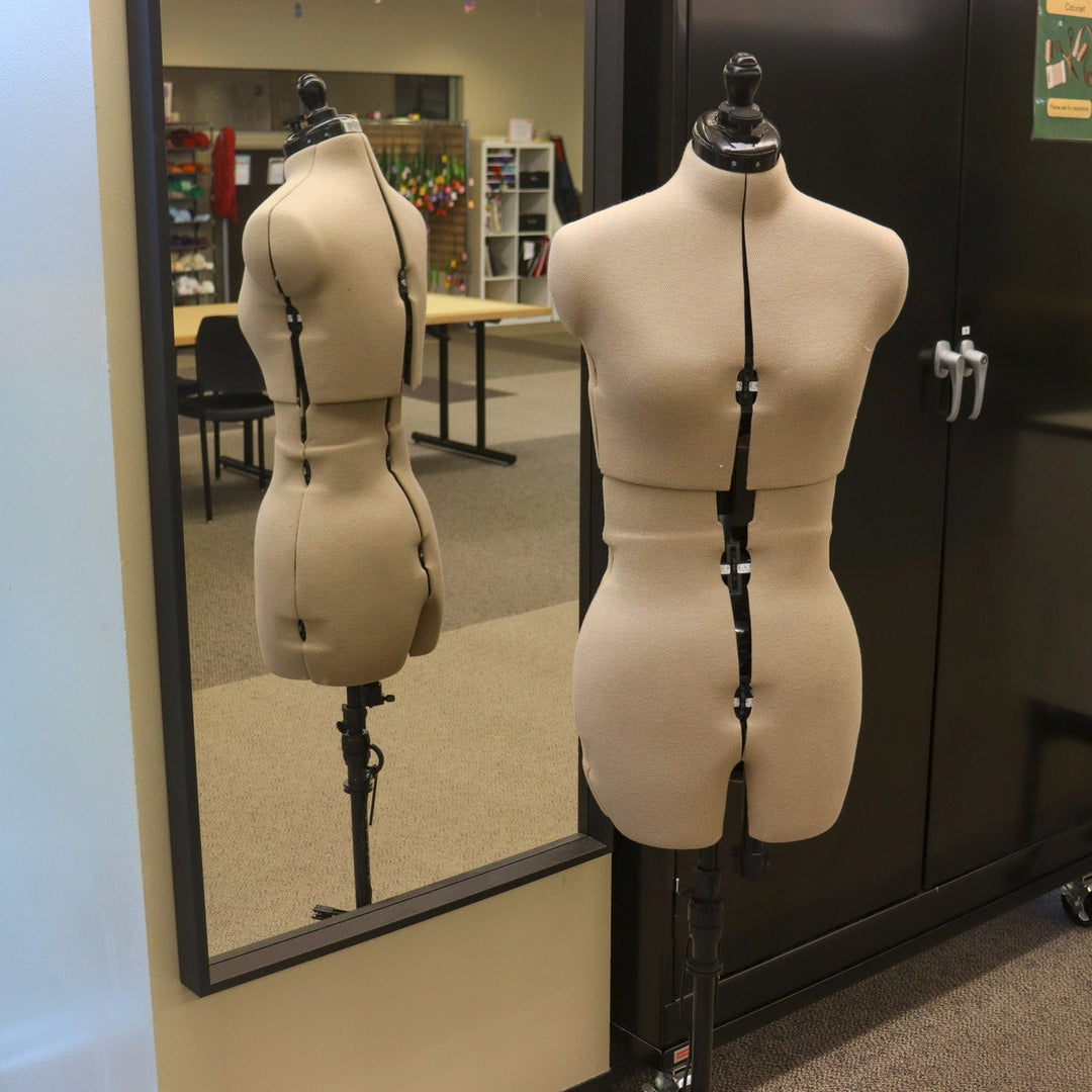 An adjustable dress form in front of a full-length mirror.