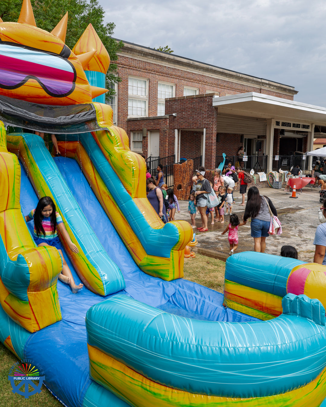 People line up to slide down a brightly colored water slide in the parking lot of Argenta Library.