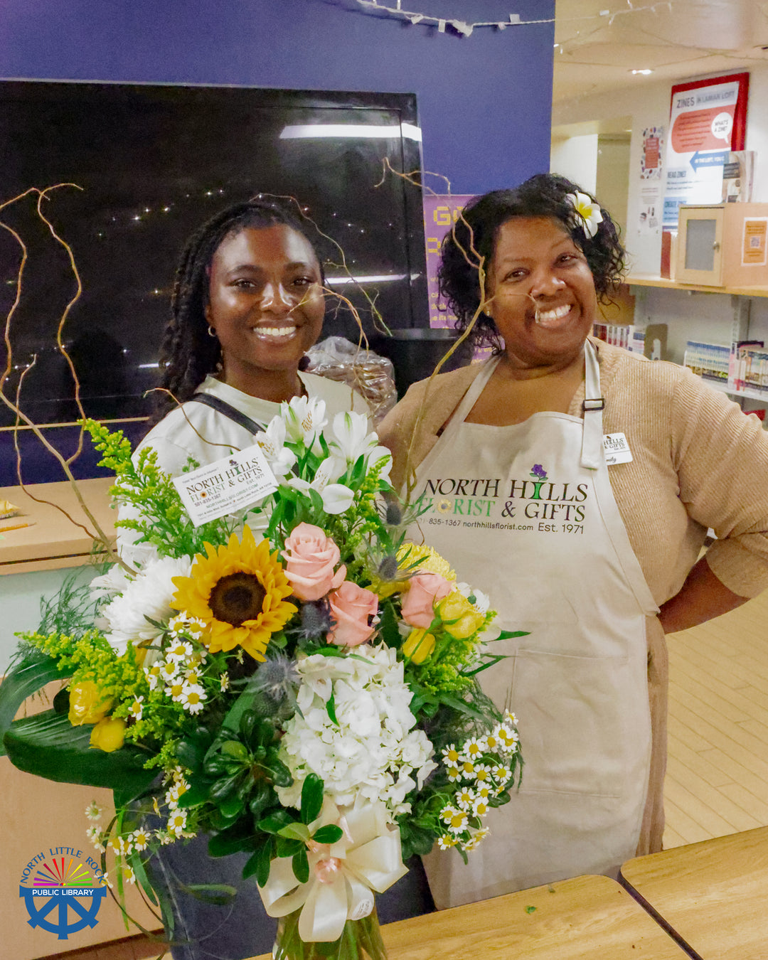 Emmily from North Hills Florist & Gifts smiles at the camera while another woman smiled and holds the floral arrangement that Emmily just completed during her demonstration.