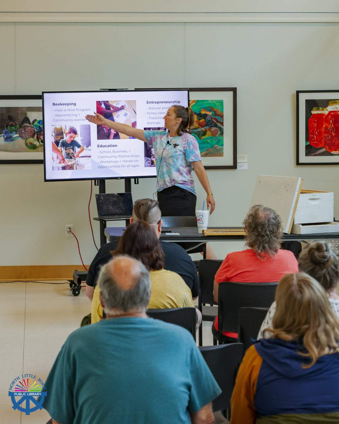Lauren from Calm and Confidence Beekeeping gestures to slides on a TV screen and talks to lecture attendees about local opportunities to get involved in beekeeping.
