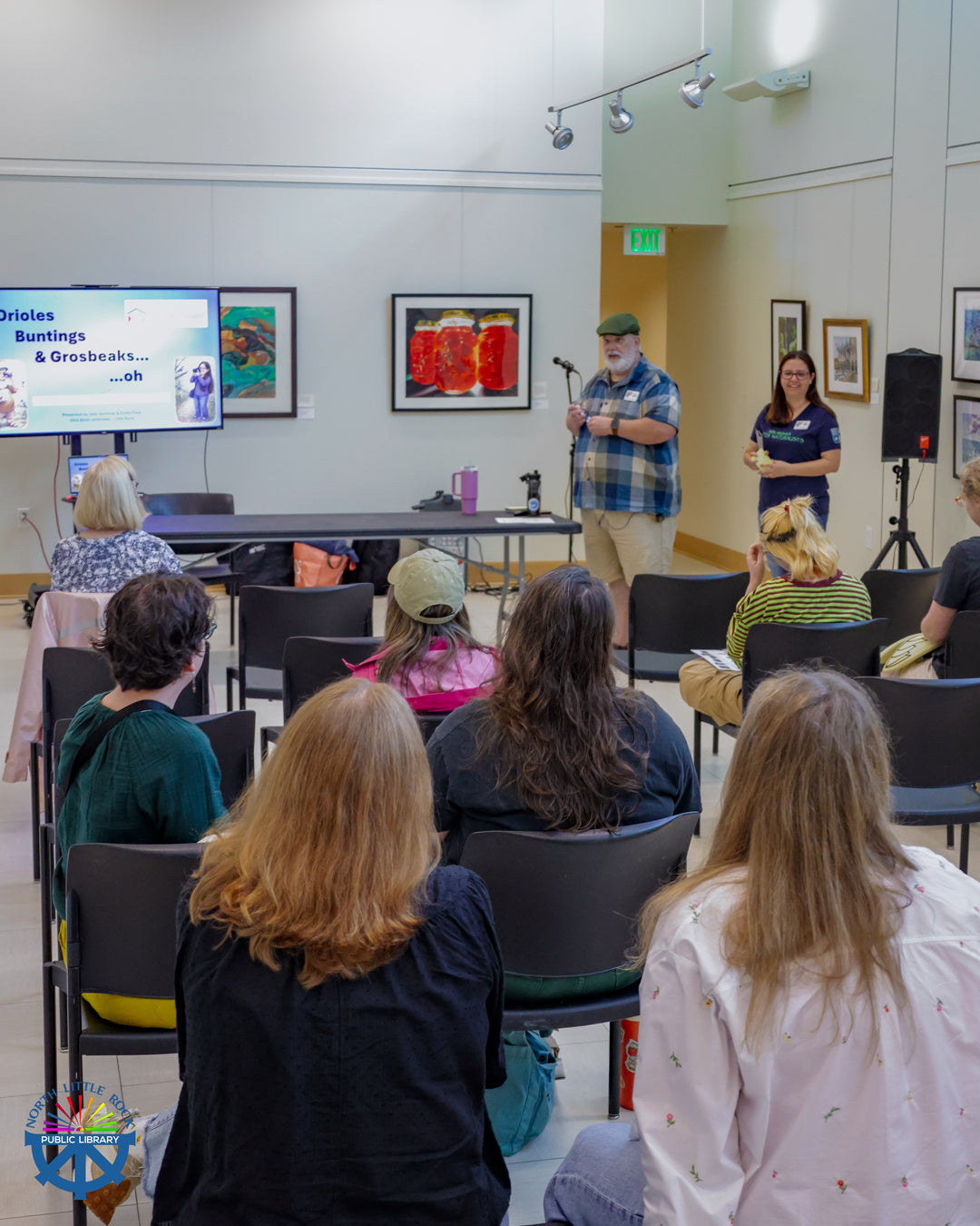 Two representatives from Wild Birds Unlimited stand at the front of a room full of seated people delivering a lecture about birding.