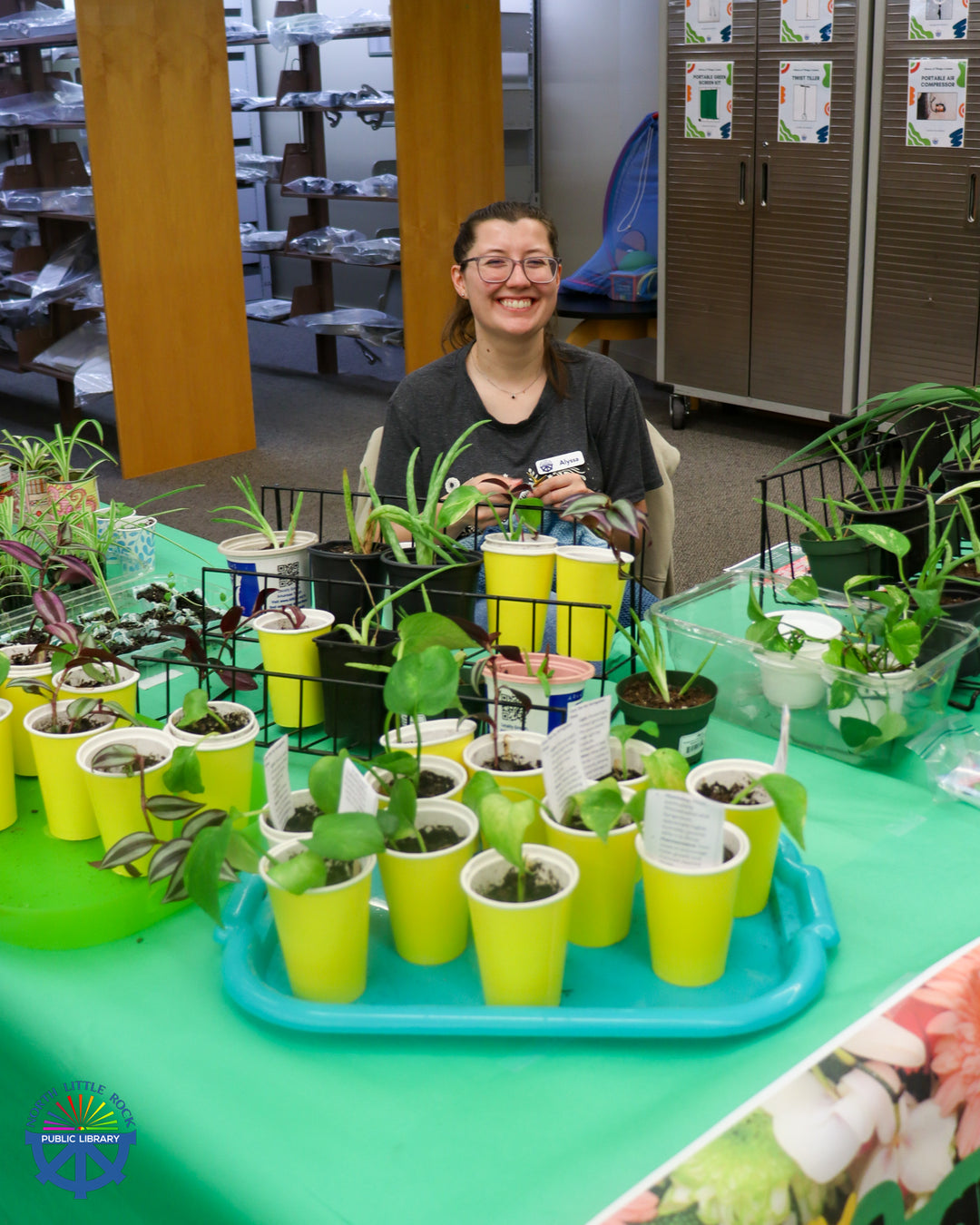 Staff member Alyssa oversees the Plant Swap table, covered in green paper and plants in colorful containers.