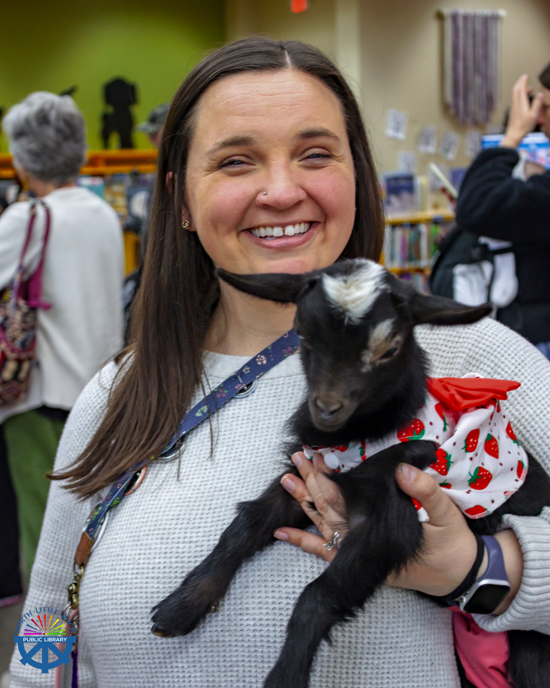 Laman children's department manager Jill holds a black baby goat wearing a white dress with red strawberries.