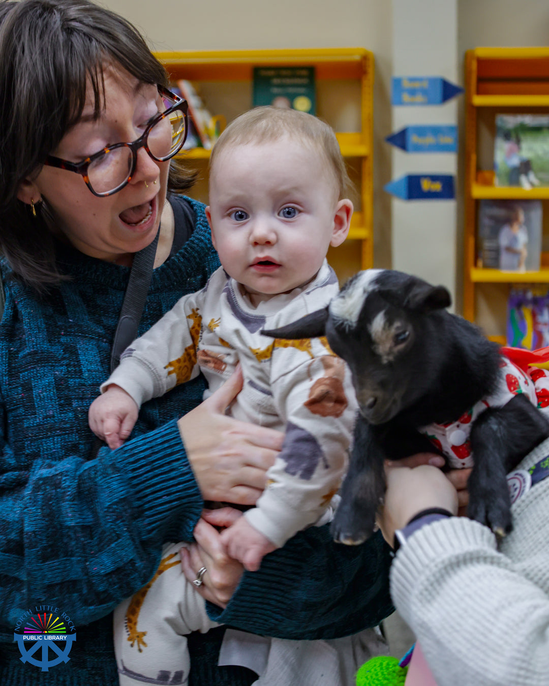 A surprised-looking woman holding a baby looks at a baby goat.