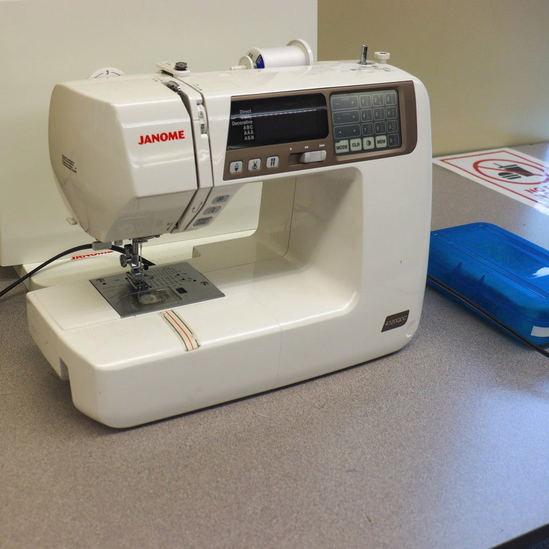 Janome sewing machine on a counter with a blue box of sewing tools.