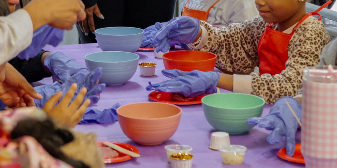 Children preparing food in bowls on a purple table.