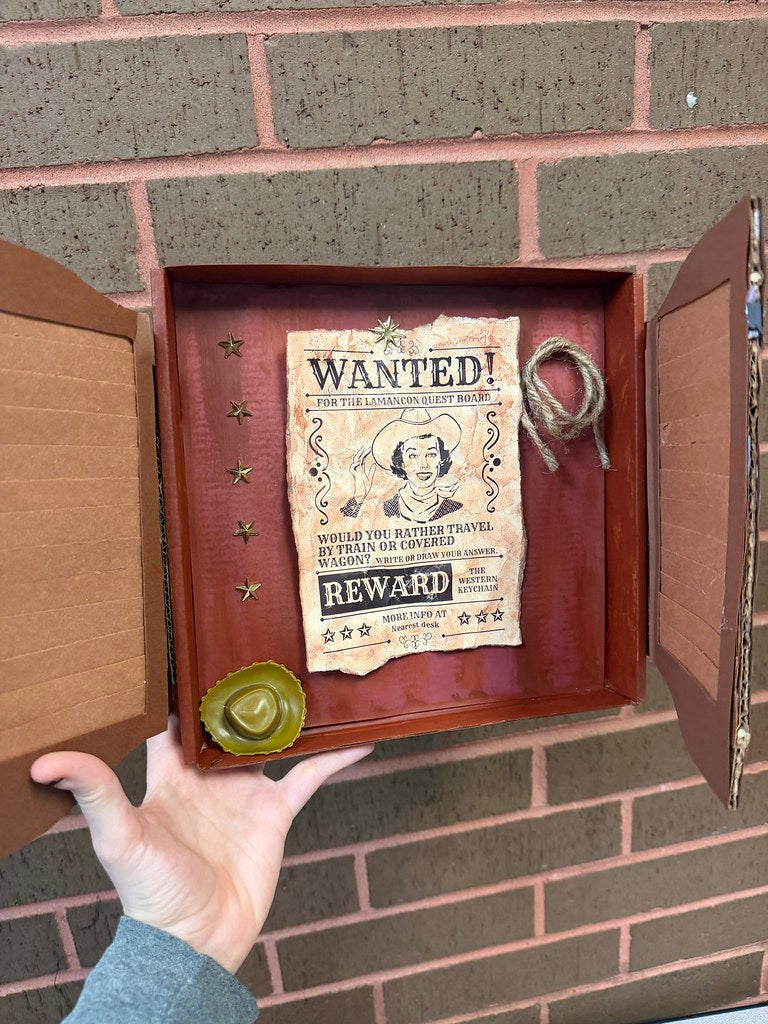 A cardboard box decorated like saloon doors. Inside, a western-style poster reading Wanted: Would you rather travel by train or covered wagon?