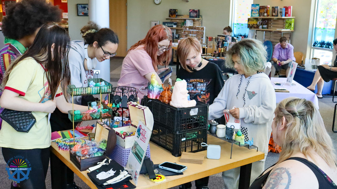Group of people gathered around a table with various dnd, gaming, and crafty gadgets items for sale.