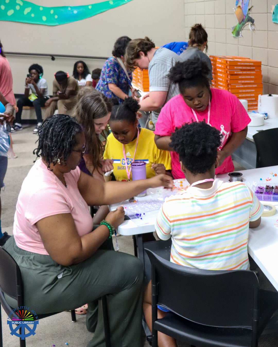 A group of people crowded around a table making bracelets.