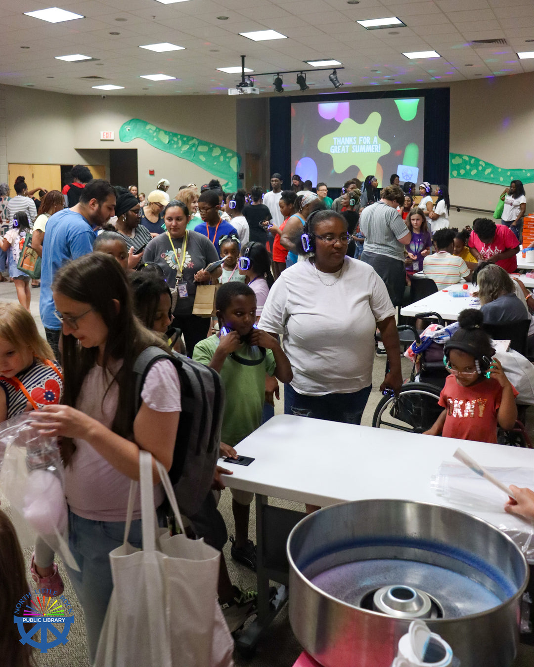 End-of-summer partygoers in the Lecture Hall. The room is full of people of all ages, some wearing lanyards or headphones.