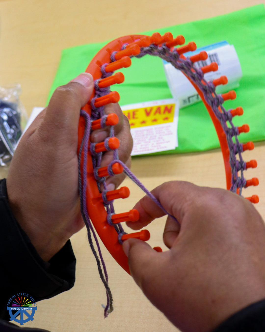 A person holding an orange circular loom with purple yarn.
