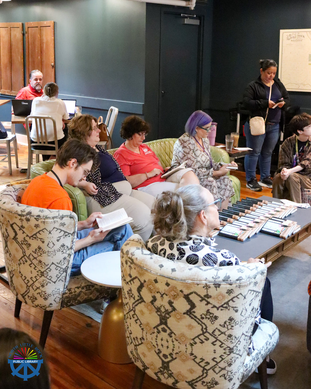 Group of people sitting at Blackberry Market with patterned chairs and a table filled with free copies of the book.