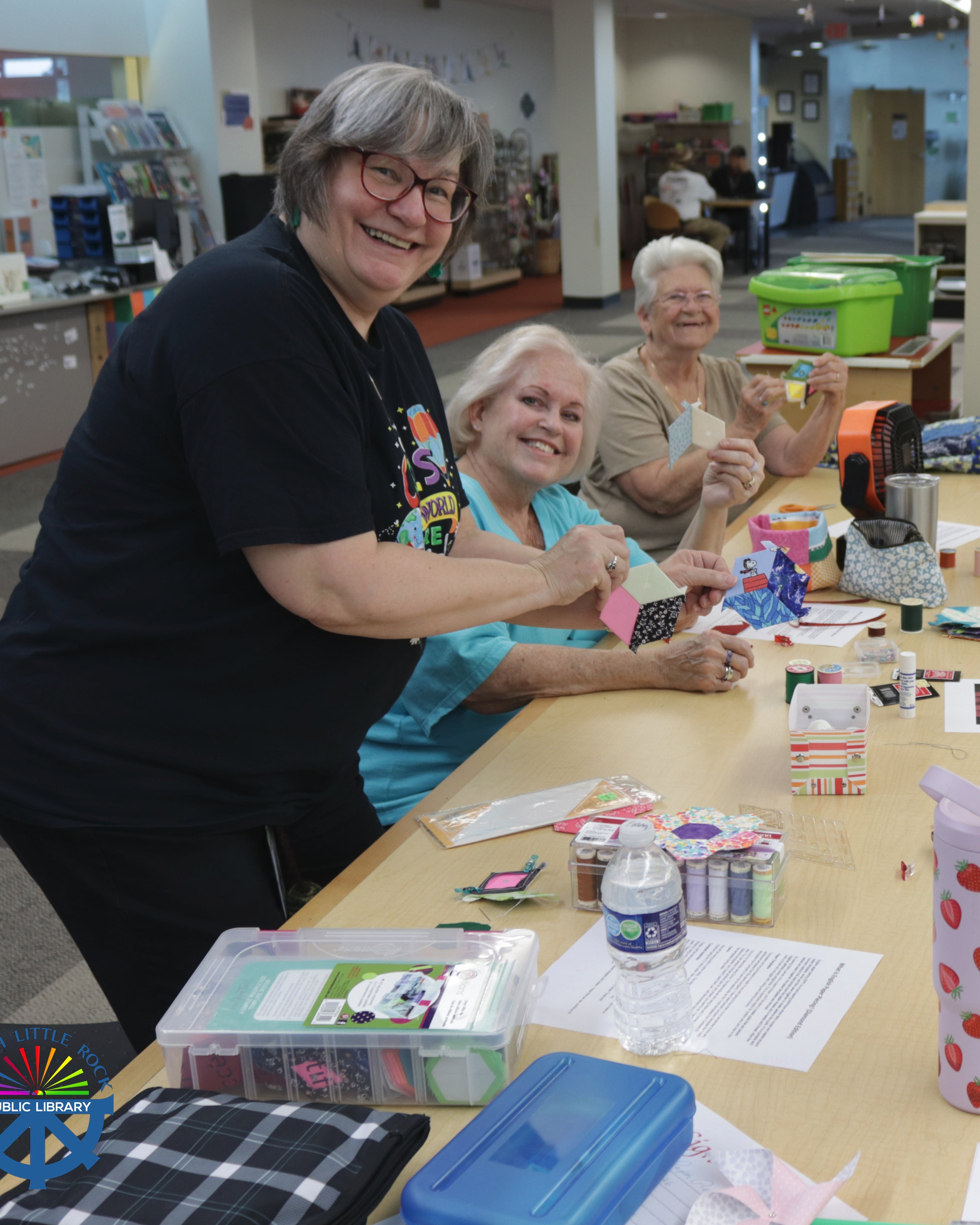 Smiling people holding up hand-sewn items.