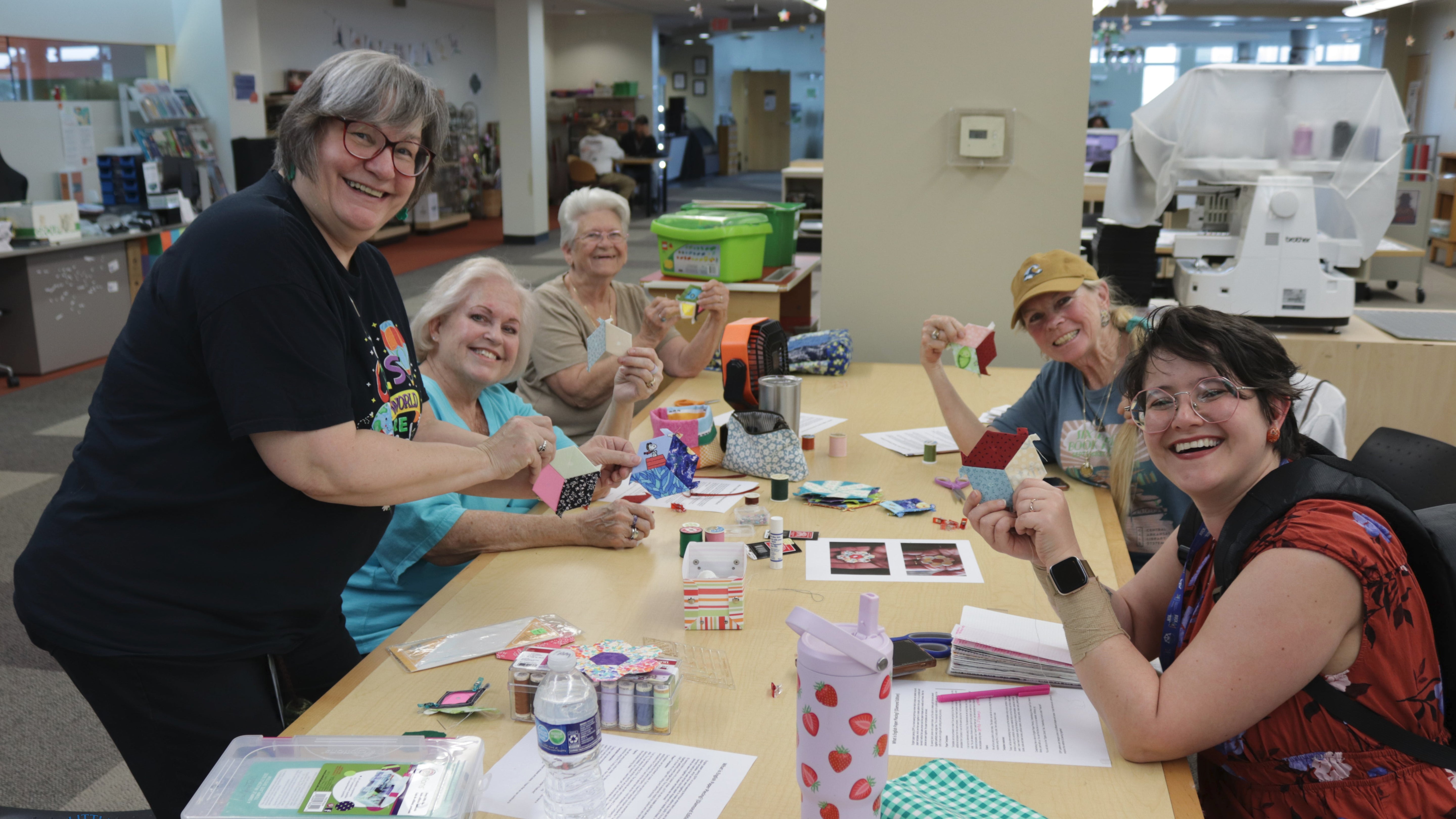 Smiling people at a table holding up hand-sewn items.