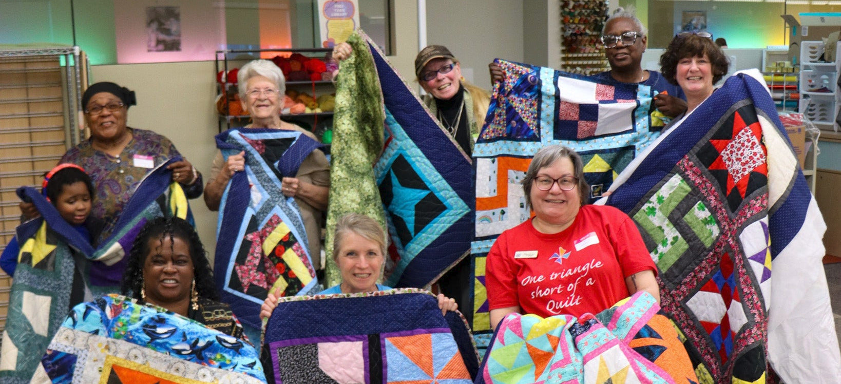 A group of people hold up colorful quilts.