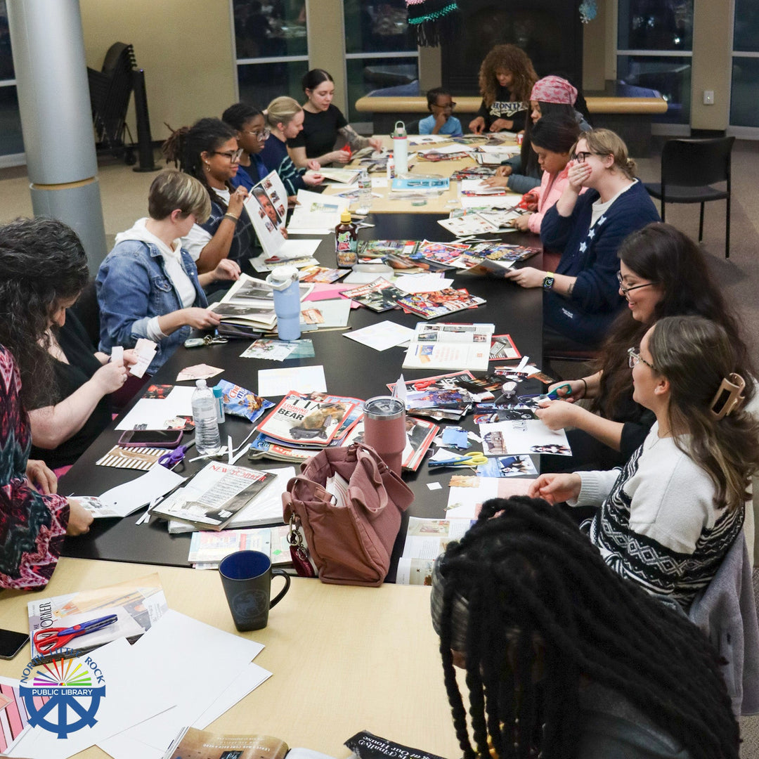 A group of people sit at a long table creating vision boards with paper and magazines.