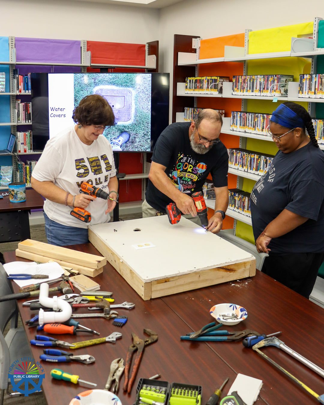 Mr. Fix-it demonstrating a drill for two library patrons at a tool workshop.