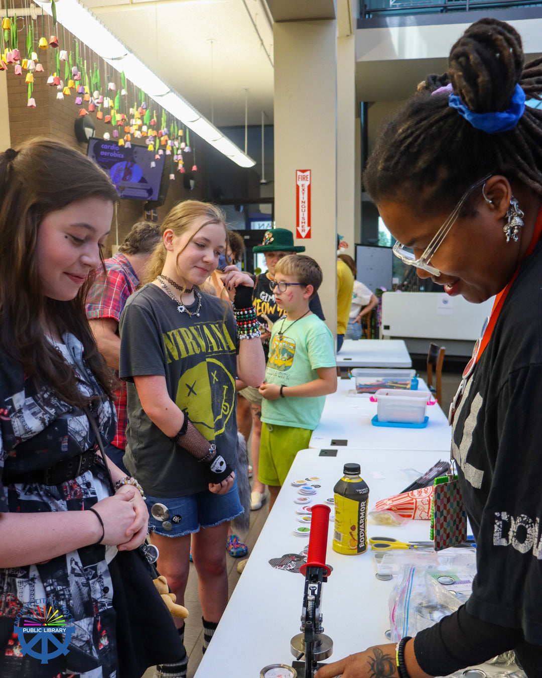 Tween department leader Drienne demonstrates the button maker to punk show attendees.