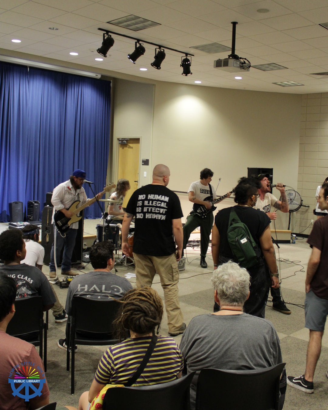 A punk band performs for a crowd of people sitting and standing.
