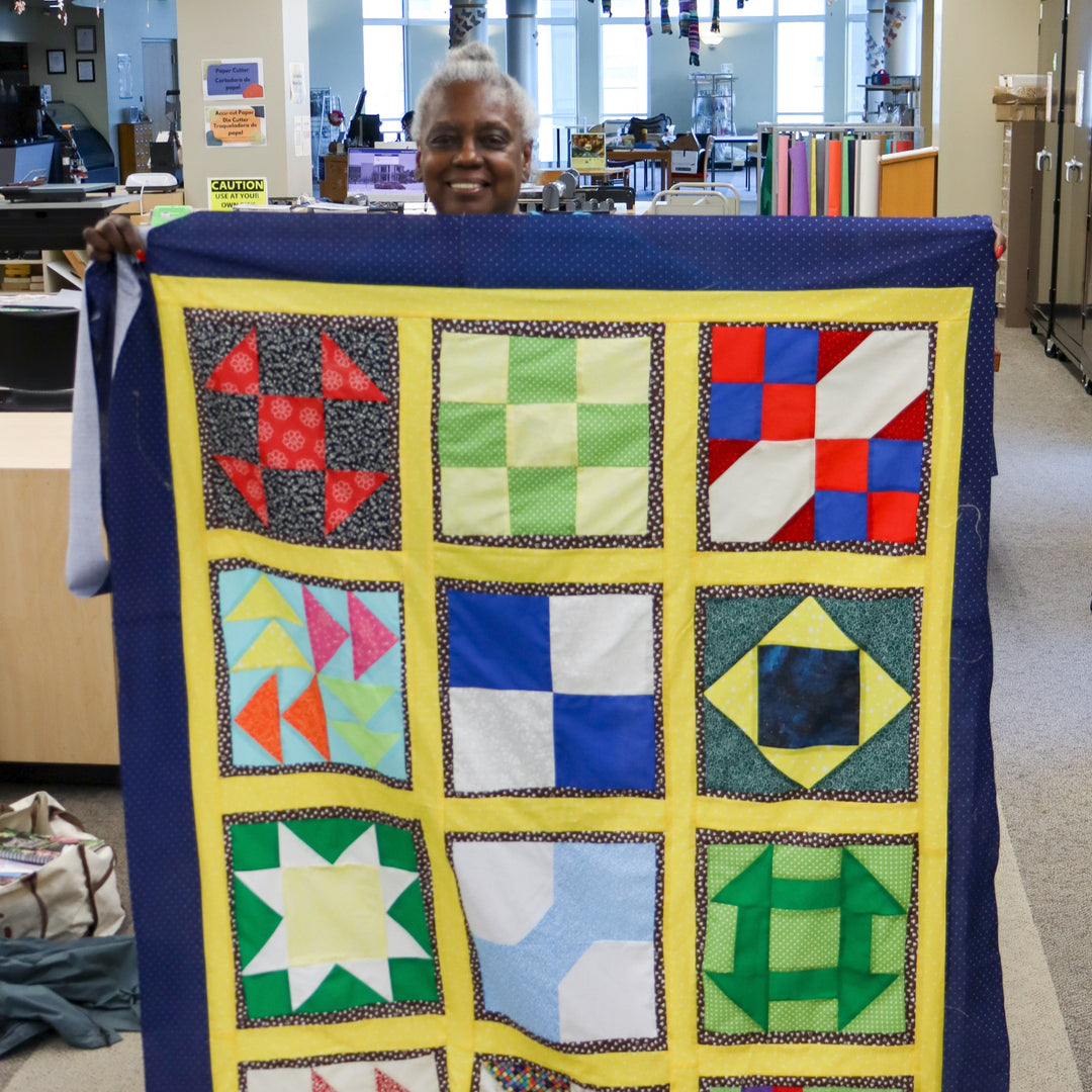 A person holds up a colorful completed quilt in the library's Makerspace.