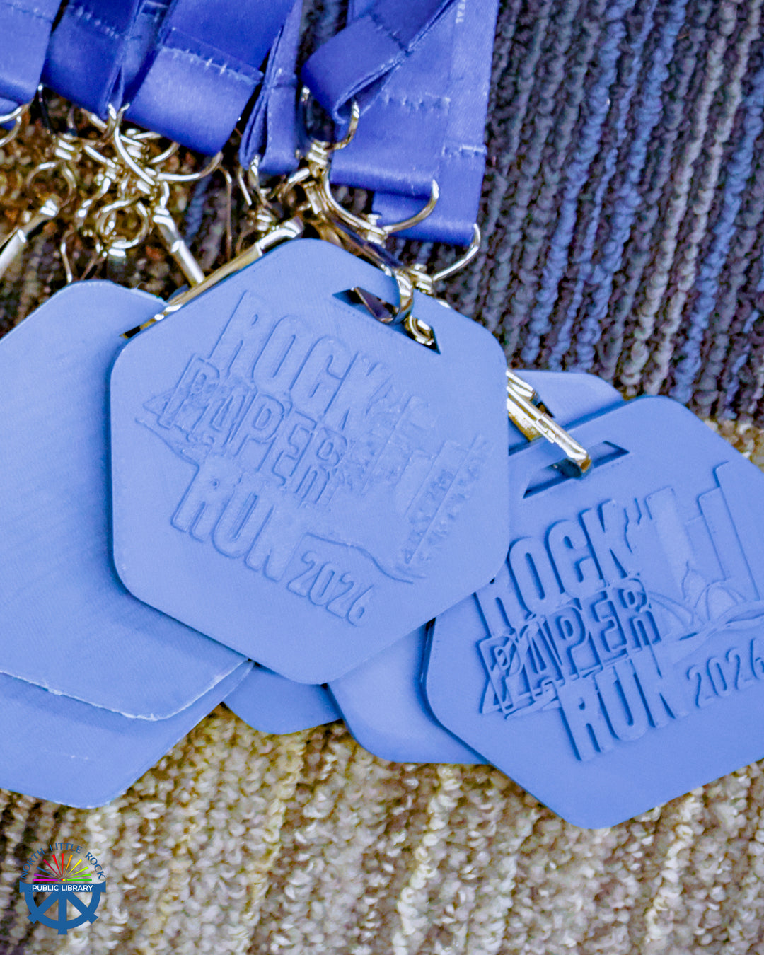 A pile of blue geometric medals with the text Rock Paper Run 2026.