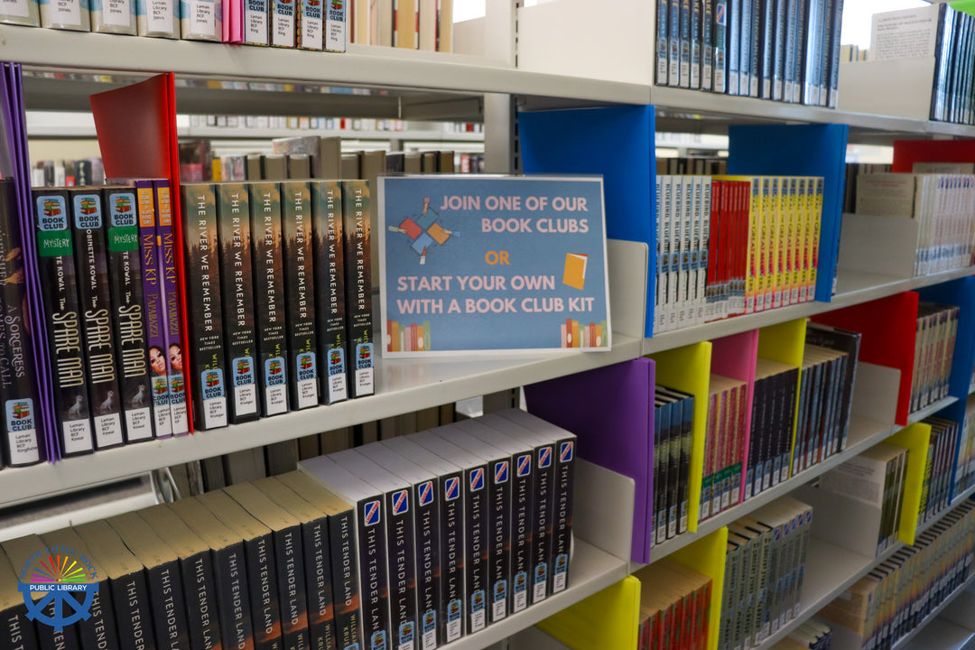 A sign on a bookshelf reading "Join one of our book clubs or start your own with a book club kit".