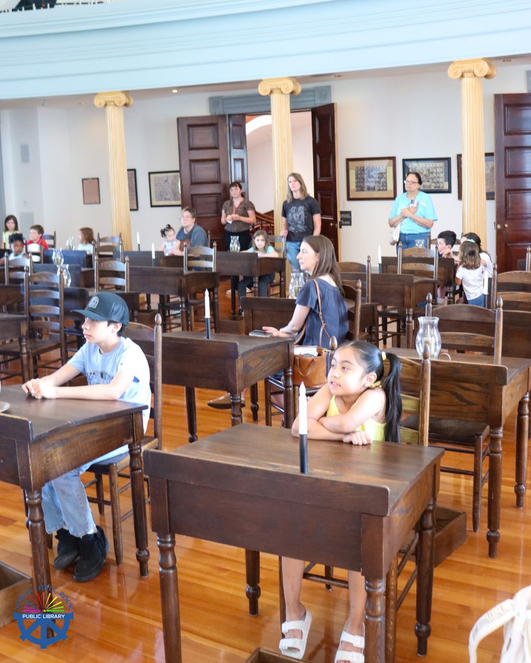 Children and caretakers sit in antique desks in a model classroom in the Old Statehouse Museum.