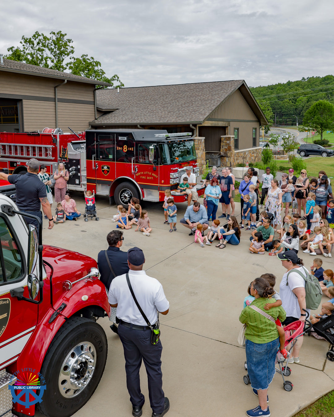 Children and families gather around red fire trucks to listen to firefighters the Burns Park Fire Station.