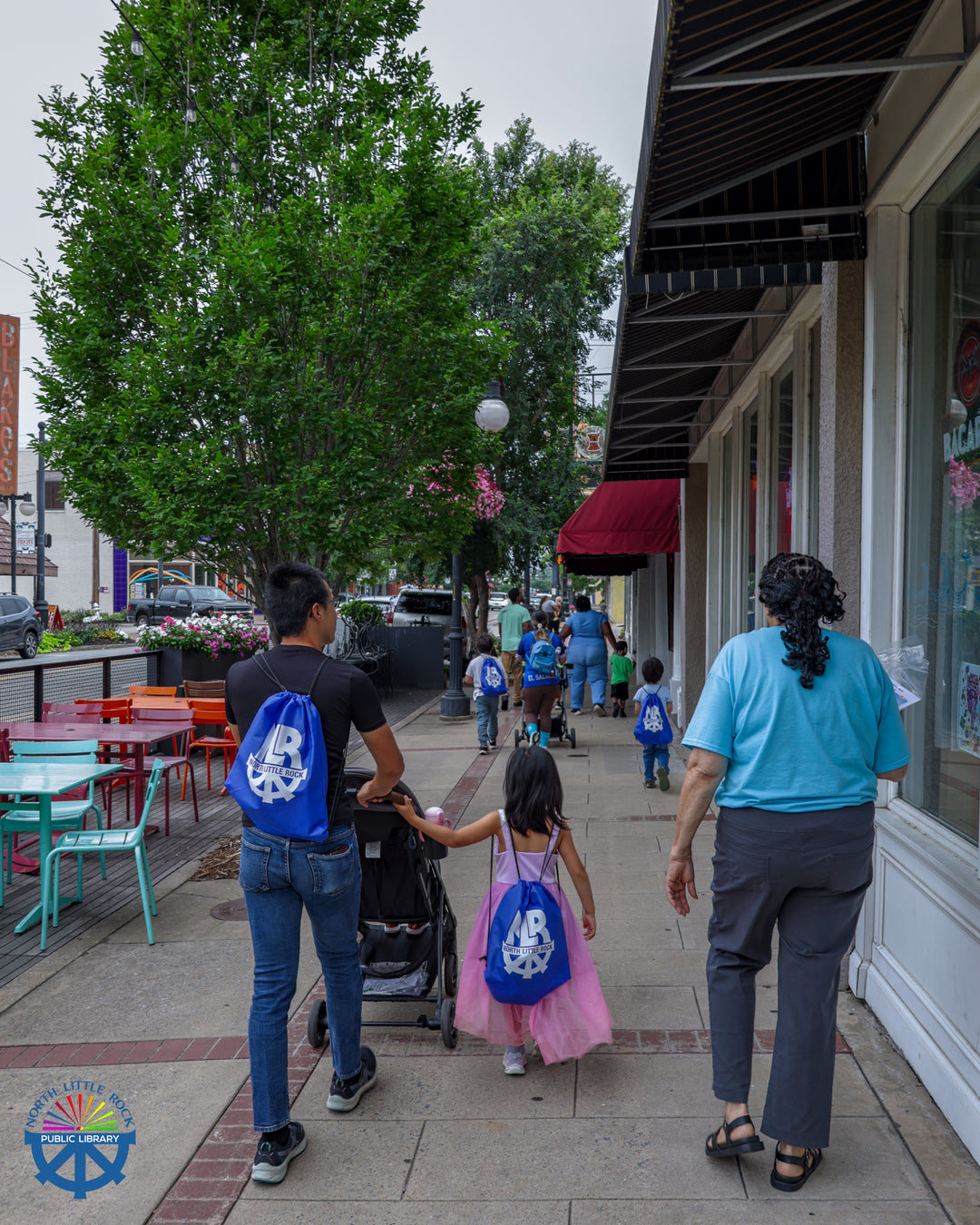 A group of people wearing blue backpacks walk own the street towards North Little Rock's City Hall.
