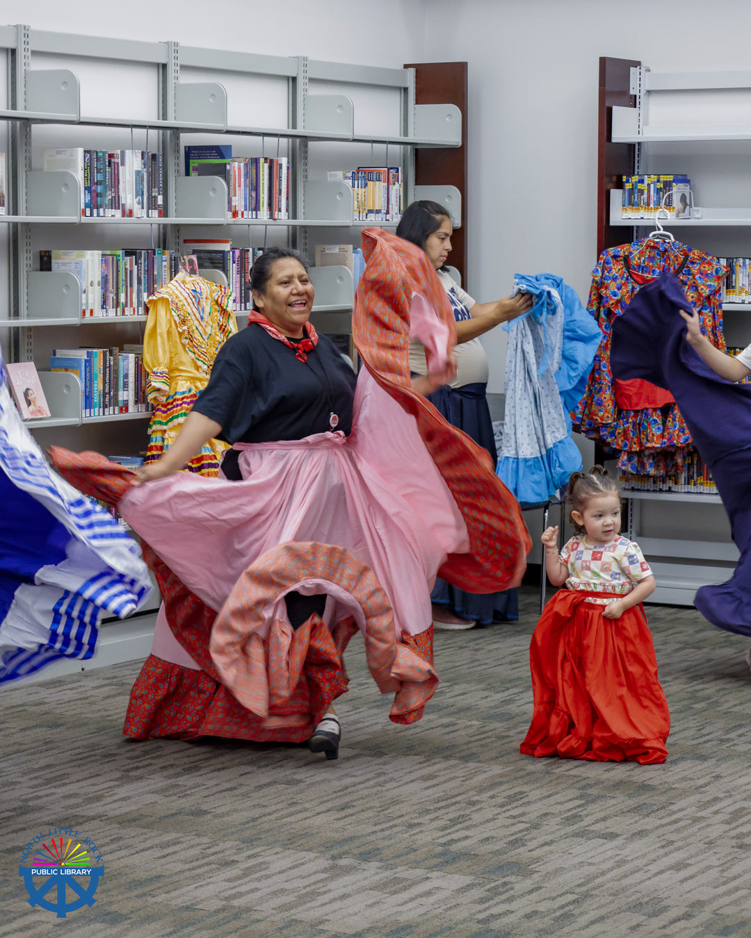 Women in colorful flowing dresses demonstrate traditional Latin American dance to a young child.